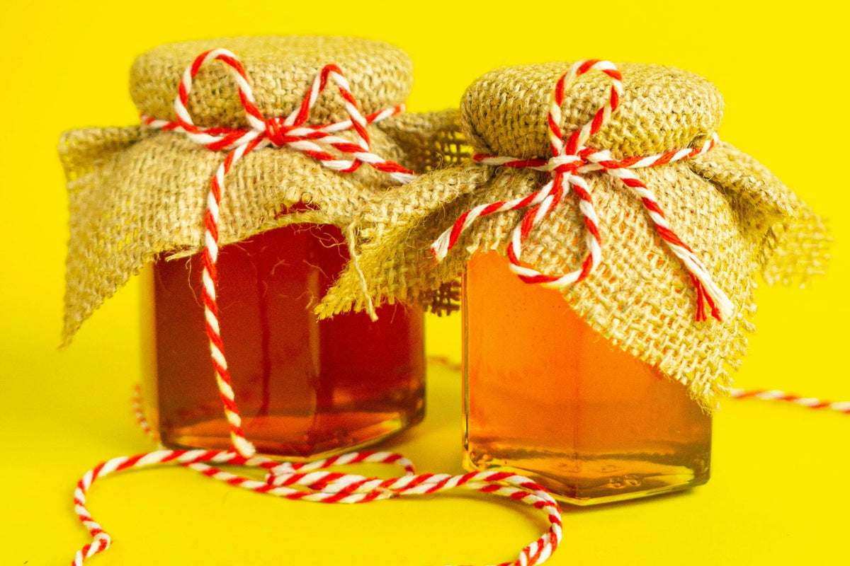 Twee potten honing feestelijk ingepakt met jute en rood-wit touw als klein cadeau